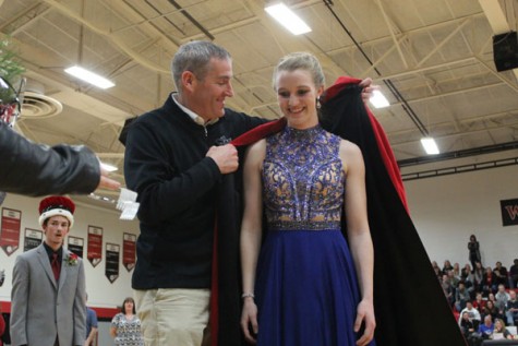 Principal Scott Buchler wrapping a cape around Snowfest Queen Madison Perrin.