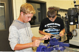 Freshman Jacob Grimes (left) and sophomore Colin Berry (right) use metal files to form the shape of a key chain in  STEM Advanced Manufacturing and Engineering class.